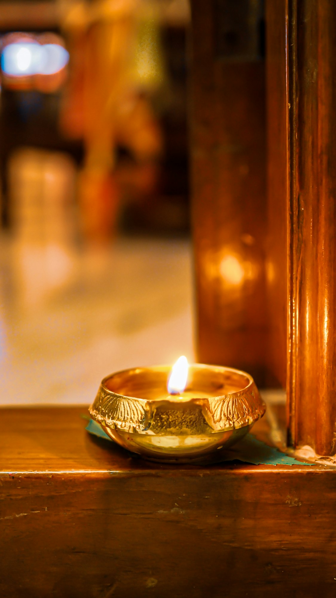 A single lit brass diya glowing on a wooden ledge