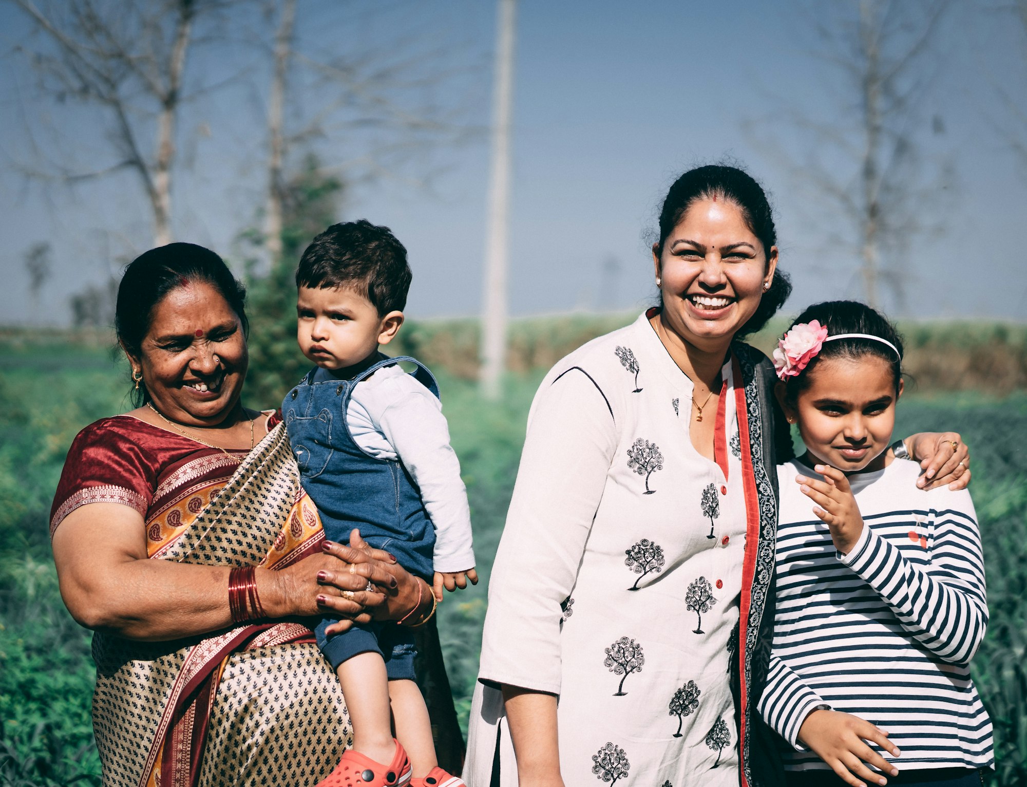 Three generations of an Indian family smiling together outdoors in a green field