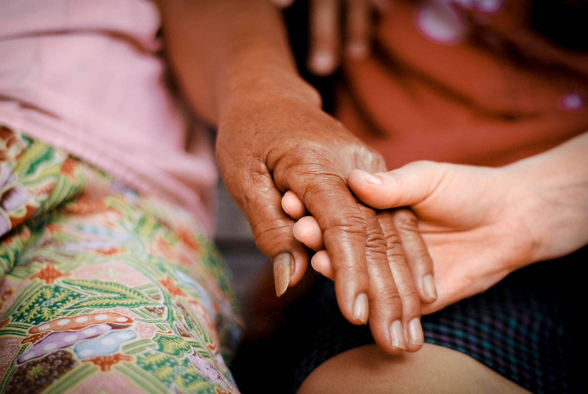 A younger hand gently holding an older person's hand